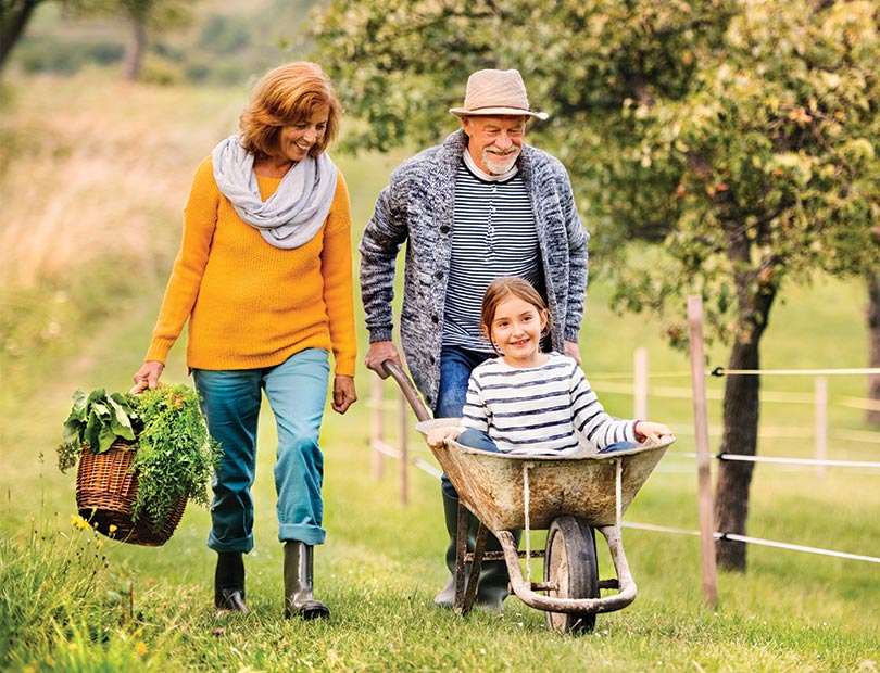 grandparents pushing their granddaughter in a wheel barrow in outdoor garden life insurance options